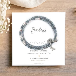 May include: A circular beaded bracelet featuring grey and silver beads arranged in a Morse code pattern. The display card includes the text Badass, the Morse code sequence, and the phrases Strong, Fearless, Unapologetically You, and Ardent Fondness.