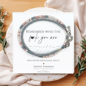 May include: A beaded bracelet featuring alternating blue and metallic silver beads, displayed on a white card with the text REMEMBER WHO THE FUCK YOU ARE AND NEVER APOLOGIZE FOR IT, along with Morse code dots and dashes and the brand name ARDENT FONDNESS.
