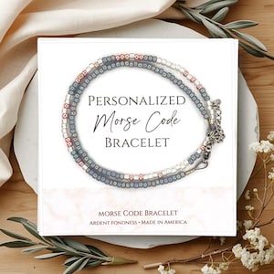 May include: A personalized Morse code bracelet with a silver clasp, presented on a white card. The bracelet features a design of small beads in shades of gray, white, and red. The card reads "PERSONALIZED Morse Code BRACELET".