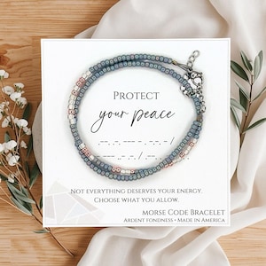 May include: A beaded Morse code bracelet with the words "PROTECT your peace" on a white card. The bracelet is gray with pink and white beads. The card also includes the text "NOT EVERYTHING DESERVES YOUR ENERGY. CHOOSE WHAT YOU ALLOW."