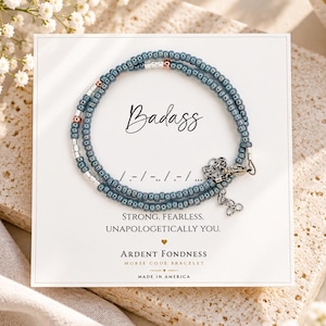 May include: A blue beaded bracelet on a white display card featuring the word Badass in script, Morse code dots and dashes, and the text Strong, Fearless, Unapologetically You, Ardent Fondness, and Made in America with a metal lobster clasp.