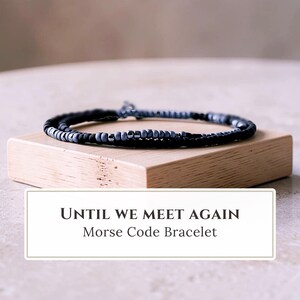 May include: A Morse code bracelet featuring alternating black and grey beads arranged in a linear pattern. The bracelet is displayed with a white rectangular label containing the black text "UNTIL WE MEET AGAIN" and "Morse Code Bracelet".