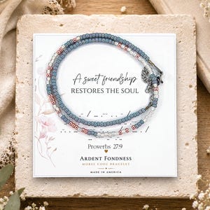 May include: A beaded bracelet featuring alternating blue, silver, and rose gold seed beads arranged in a Morse code pattern. The bracelet is displayed on a white card printed with the text A sweet friendship RESTORES THE SOUL Proverbs 27:9.