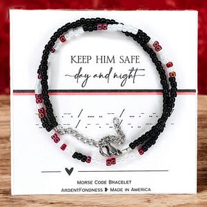 May include: A black and white beaded bracelet with red beads, on a white card with the text "KEEP HIM SAFE - day and night" and "MORSE CODE BRACELET - ARDENTFONDNESS - MADE IN AMERICA".