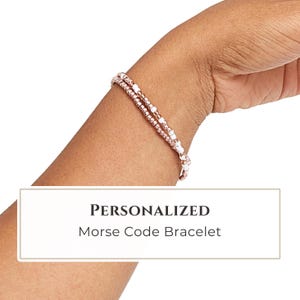 May include: A delicate bracelet featuring a repeating pattern of metallic rose gold and small white beads. The text PERSONALIZED Morse Code Bracelet is displayed in a white rectangular box positioned below the beaded jewelry piece.