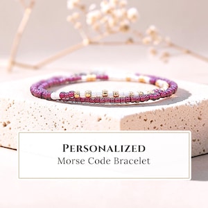 May include: A delicate beaded bracelet featuring a pattern of deep magenta, white, and metallic gold seed beads arranged in a sequence. The text PERSONALIZED Morse Code Bracelet is displayed in a rectangular frame below the jewelry piece.
