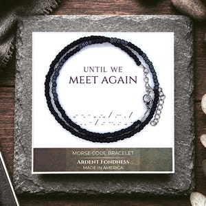 May include: A black beaded Morse code bracelet displayed on a white card featuring the text UNTIL WE MEET AGAIN, a Morse code sequence, and the words MORSE CODE BRACELET, ARDENT FONDNESS, and MADE IN AMERICA. The bracelet has a silver metal clasp.