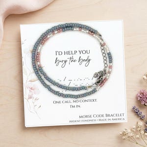 May include: A Morse code bracelet with a message, displayed on a card. The bracelet is made of small, blue, white, and pink beads. The card reads "I'd help you bury the body" and "One call. No context. I'm in."