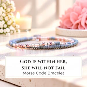 May include: A Morse code bracelet featuring alternating blue, silver, and rose gold beads. The bracelet is displayed with text that reads: GOD IS WITHIN HER, SHE WILL NOT FAIL. Morse Code Bracelet. The design consists of small, round beads.