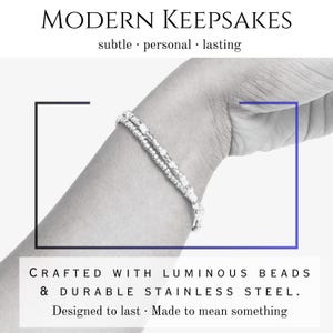 Peut inclure: Un bracelet argent&eacute; avec des perles lumineuses et de l'acier inoxydable. L'image comprend le texte "MODERN KEEPSAKES" et "CRAFTED WITH LUMINOUS BEADS & DURABLE STAINLESS STEEL. Designed to last - Made to mean something."
