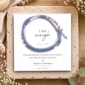 May include: A Morse code bracelet made of blue and metallic pink beads on a white display card. The card features the text I AM enough, the Morse code sequence, and the phrase A REMINDER ON THE DAYS YOU FORGET. YOU ARE ALREADY ENOUGH.