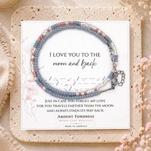 May include: A beaded bracelet featuring alternating blue, silver, and rose gold seed beads on a display card. The card displays the text I LOVE YOU TO THE moon and back, Morse code symbols, and the phrase JUST IN CASE YOU FORGET, MY LOVE.