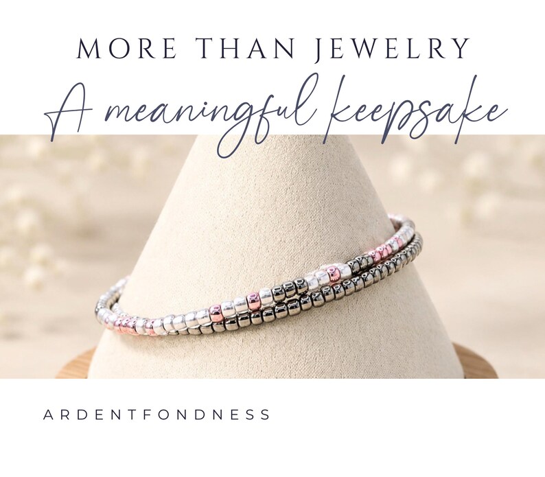K&ouml;nnte beinhalten: Ein zweireihiges Perlenarmband mit kleinen metallischen silbernen, ros&eacute;goldenen und dunkelgrauen Perlen. Der Text MORE THAN JEWELRY A meaningful keepsake und ARDENTFONDNESS ist &uuml;ber und unter dem Armband auf dem Bild zu sehen.