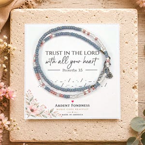 May include: A delicate beaded bracelet featuring small blue, clear, and metallic rose gold beads arranged in a pattern. The bracelet is displayed on a white card printed with the text TRUST IN THE LORD with all your heart Proverbs 3:5.
