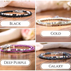 May include: Four beaded bracelets featuring small round beads in black, gold, deep purple, and galaxy colorways. Each bracelet incorporates white and metallic silver accent beads, a thin cord structure, and a silver-toned metal lobster claw clasp.