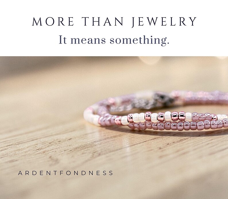 May include: A beaded bracelet featuring small, metallic rose gold and opaque white glass seed beads. The text MORE THAN JEWELRY It means something. and ARDENTFONDNESS are printed in black on the white background above and below the bracelet.