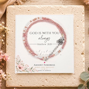 May include: A Morse code bracelet featuring metallic rose gold and white beads on a display card. The card text reads: GOD IS WITH YOU always Matthew 28:20, Ardent Fondness Morse Code Bracelet, and Made in America. The bracelet has a silver-toned metal chain extender.
