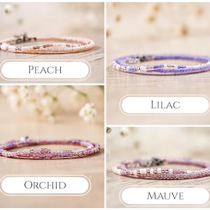 K&ouml;nnte beinhalten: Vier d&uuml;nne Perlenarmb&auml;nder in den Farben Pfirsich, Flieder, Orchidee und Mauve. Jedes Armband besteht aus kleinen, gleichm&auml;&szlig;igen Glasperlen in verschiedenen Schattierungen der jeweiligen Farbe, mit einem Metallverschluss und der Beschriftung PEACH, LILAC, ORCHID oder MAUVE.