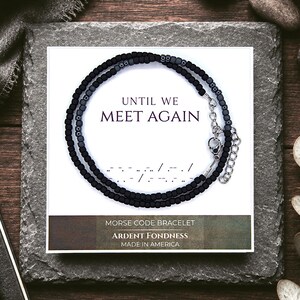 May include: A black beaded Morse code bracelet displayed on a white card featuring the text UNTIL WE MEET AGAIN, a Morse code sequence, and the words MORSE CODE BRACELET, ARDENT FONDNESS, and MADE IN AMERICA. The bracelet has a silver metal clasp.