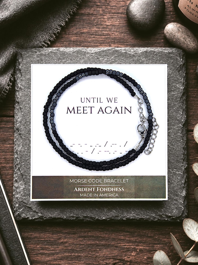 May include: A black beaded Morse code bracelet displayed on a white card featuring the text UNTIL WE MEET AGAIN, a Morse code sequence, and the words MORSE CODE BRACELET, ARDENT FONDNESS, and MADE IN AMERICA. The bracelet has a silver metal clasp.