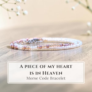 May include: A delicate bracelet crafted from small white and metallic rose gold beads arranged in a pattern representing Morse code. The text A PIECE OF MY HEART IS IN HEAVEN Morse Code Bracelet is displayed below the jewelry item.