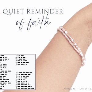 K&ouml;nnte beinhalten: Ein zweireihiges Perlenarmband mit metallisch ros&eacute;goldenen und undurchsichtigen wei&szlig;en Saatperlen. Der Text A QUIET REMINDER of faith steht oben, und unten links ist eine Referenztabelle f&uuml;r den Morsecode abgebildet.