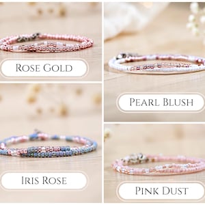 K&ouml;nnte beinhalten: Eine Sammlung von vier Perlenarmb&auml;ndern mit kleinen, runden, metallischen und matten Perlen in verschiedenen Farbkombinationen. Die Armb&auml;nder sind mit Rose Gold, Pearl Blush, Iris Rose und Pink Dust beschriftet und haben einen silberfarbenen Verschluss.