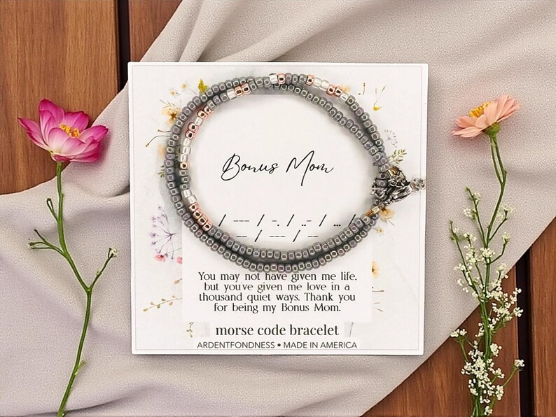 May include: A beaded bracelet with a Morse code design, presented on a card that reads "Bonus Mom." The bracelet is gray and rose gold, with a decorative clasp. The card includes a message and the words "Morse code bracelet."