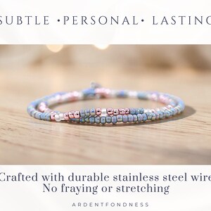 May include: A delicate beaded bracelet in shades of blue, pink, and rose gold. The bracelet is made with small, round beads strung on durable stainless steel wire. The text reads "SUBTLE &bull; PERSONAL &bull; LASTING" and "Crafted with durable stainless steel wire No fraying or stretching".