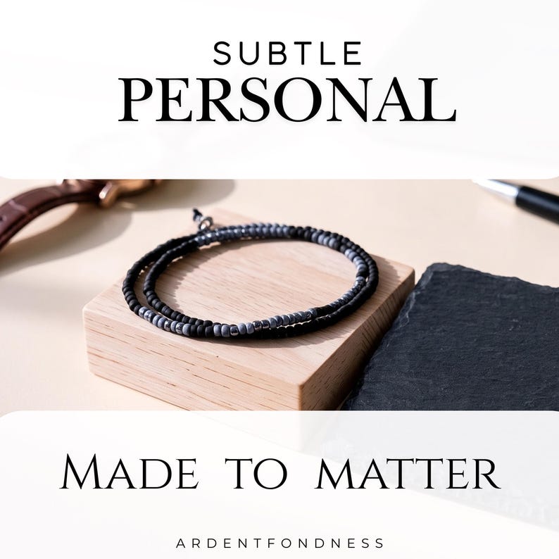 May include: A wrap bracelet featuring alternating matte black and metallic grey beads. The text SUBTLE PERSONAL is printed at the top, and MADE TO MATTER ARDENTFONDNESS is printed at the bottom. The bracelet is coiled in a circular shape.