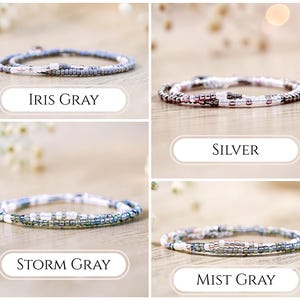 K&ouml;nnte beinhalten: Vier zarte Perlenarmb&auml;nder aus kleinen, runden Glasperlen in verschiedenen Farbpaletten. Die Armb&auml;nder sind mit Iris Gray, Silver, Storm Gray und Mist Gray beschriftet und zeigen Kombinationen aus wei&szlig;en, grauen, metallischen und bl&auml;ulichen Perlen.