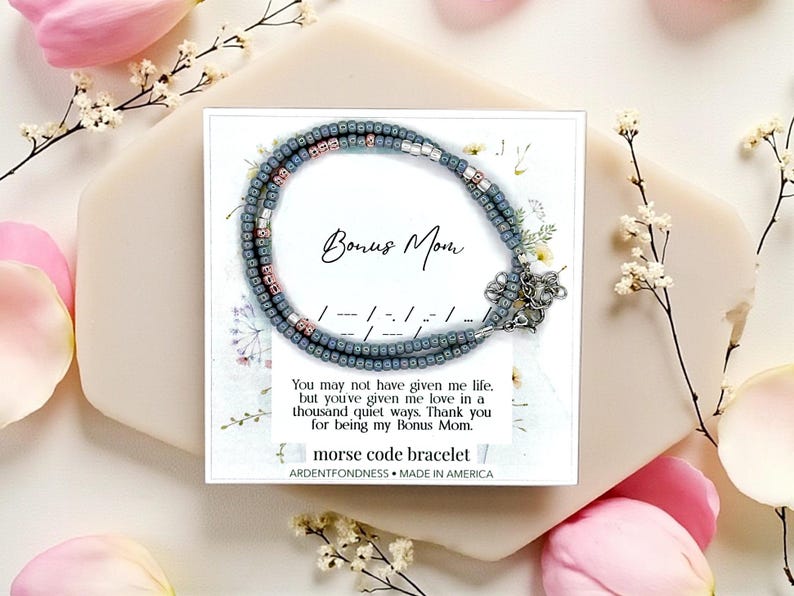 May include: A gray beaded Morse code bracelet with a silver clasp, presented on a card that reads "Bonus Mom." The bracelet features pink and white beads. The card includes a message and the words "Morse code bracelet" and "Made in America."