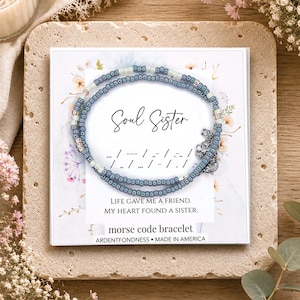 May include: A Morse code bracelet featuring blue and white seed beads on a display card. The card displays the text Soul Sister, Morse code dots and dashes, and the phrase Life gave me a friend. My heart found a sister. It includes a metal clasp.