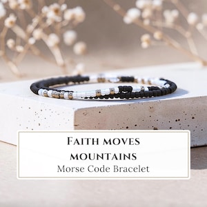 May include: A Morse code bracelet featuring a sequence of matte black, white, and metallic beads arranged in a circular pattern. The text "FAITH MOVES MOUNTAINS Morse Code Bracelet" is displayed in a rectangular frame below the jewellery piece.