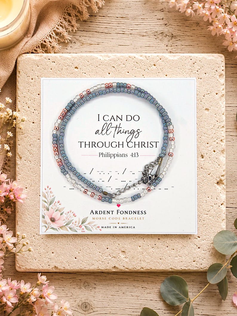 May include: A beaded bracelet featuring small blue, pink, and clear glass beads arranged in a circular pattern on a white display card. The card displays the text I CAN DO all things THROUGH CHRIST Philippians 4:13 and Morse code symbols.