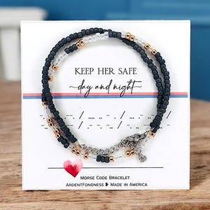 Peut inclure: Un bracelet de code Morse perl&eacute; avec le message "Keep Her Safe day and night" sur une carte blanche. Le bracelet comporte des perles noires, transparentes et dor&eacute;es. Un c&oelig;ur rouge et les mots "Morse Code Bracelet" sont &eacute;galement visibles.