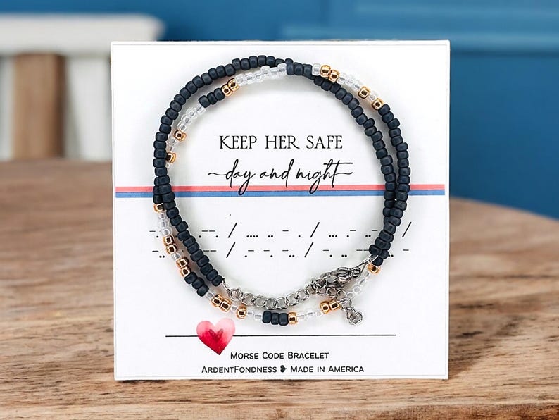 Peut inclure: Un bracelet de code Morse perl&eacute; avec le message "Keep Her Safe day and night" sur une carte blanche. Le bracelet comporte des perles noires, transparentes et dor&eacute;es. Un c&oelig;ur rouge et les mots "Morse Code Bracelet" sont &eacute;galement visibles.