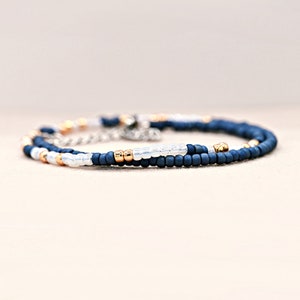 Peut inclure: Un bracelet de perles d&eacute;licat avec des perles bleu marine, dor&eacute;es et blanches. Le bracelet est compos&eacute; de petites perles rondes enfil&eacute;es ensemble, avec un fermoir en cha&icirc;ne argent&eacute;e. Le design est simple et &eacute;l&eacute;gant.