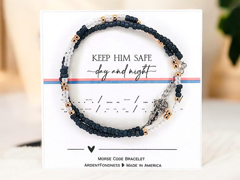 Peut inclure: Un bracelet en code Morse avec des perles bleues marine, transparentes et dor&eacute;es. Le bracelet est pr&eacute;sent&eacute; sur une carte blanche avec le texte "KEEP HIM SAFE day and night". La carte indique &eacute;galement "Morse Code Bracelet".