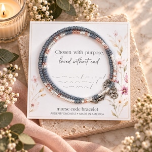May include: A Morse code bracelet featuring small grey, rose gold, and silver beads arranged on a display card. The card displays the text Chosen with purpose, loved without end, a Morse code sequence, and the words morse code bracelet.