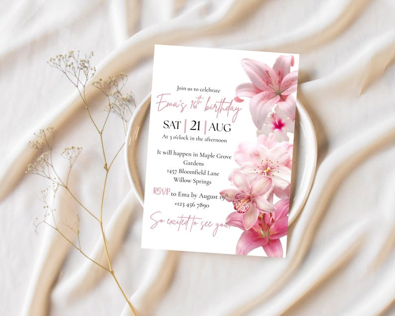 May include: A white invitation card with pink text and floral accents, announcing Ema's 16th birthday on August 21st. The card includes event details and an RSVP. The design features pink lilies and is set on a white plate and fabric.