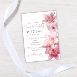 May include: A white invitation card with pink floral accents and text. The invitation reads "Ema's 1st birthday" with the date, time, and location. A white ribbon is draped across the top and bottom of the card.