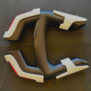 May include: A black and grey object with white and red detailing. The object features a curved handle and two opposing arms, each with a white, angular tip. The design is symmetrical and appears to be made of plastic or a similar material.
