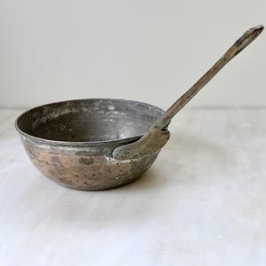 May include: A vintage copper ladle with a long handle. The ladle has a worn, aged patina and is made of solid copper.