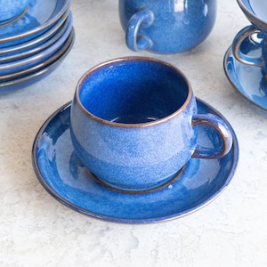 May include: A blue ceramic teacup and saucer set. The cup and saucer have a speckled glaze and a dark blue rim.