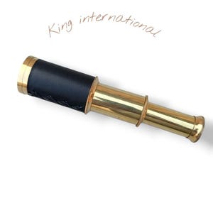 May include: A brass and black telescope with the text "King international" in cursive. The telescope has a black leather grip and gold-colored accents. The telescope is a vintage nautical item.