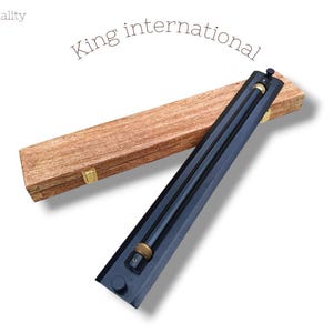 Puede incluir: Un instrumento negro y dorado con una caja de madera. El instrumento tiene un cuerpo largo y recto con una pieza dorada circular en el medio. La caja de madera es rectangular y tiene un cierre dorado. El texto "King international" está arqueado sobre el instrumento.