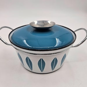 Peut inclure: Une casserole vintage en émail avec un couvercle bleu turquoise et un corps blanc orné de motifs de feuilles turquoise. Elle est dotée de deux poignées argentées et d'un petit bouton argenté sur le couvercle. Pour cuisiner et servir.