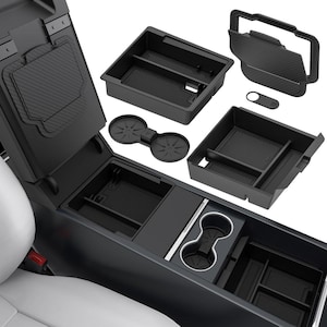 May include: A collection of black car interior organizers and accessories. Includes various trays, cup holders, and a console lid cover with a carbon fiber pattern. The items are designed to fit inside a car's center console and other storage areas.