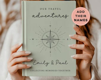 May include: A sage green hardcover journal with the text OUR TRAVEL adventures, a compass rose graphic, the names Emily & Paul, and the text COLLECTING MEMORIES TOGETHER. A circular pink badge on the cover reads ADD THEIR NAMES.